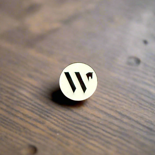Round white pin with Wellington International branding on a wooden surface