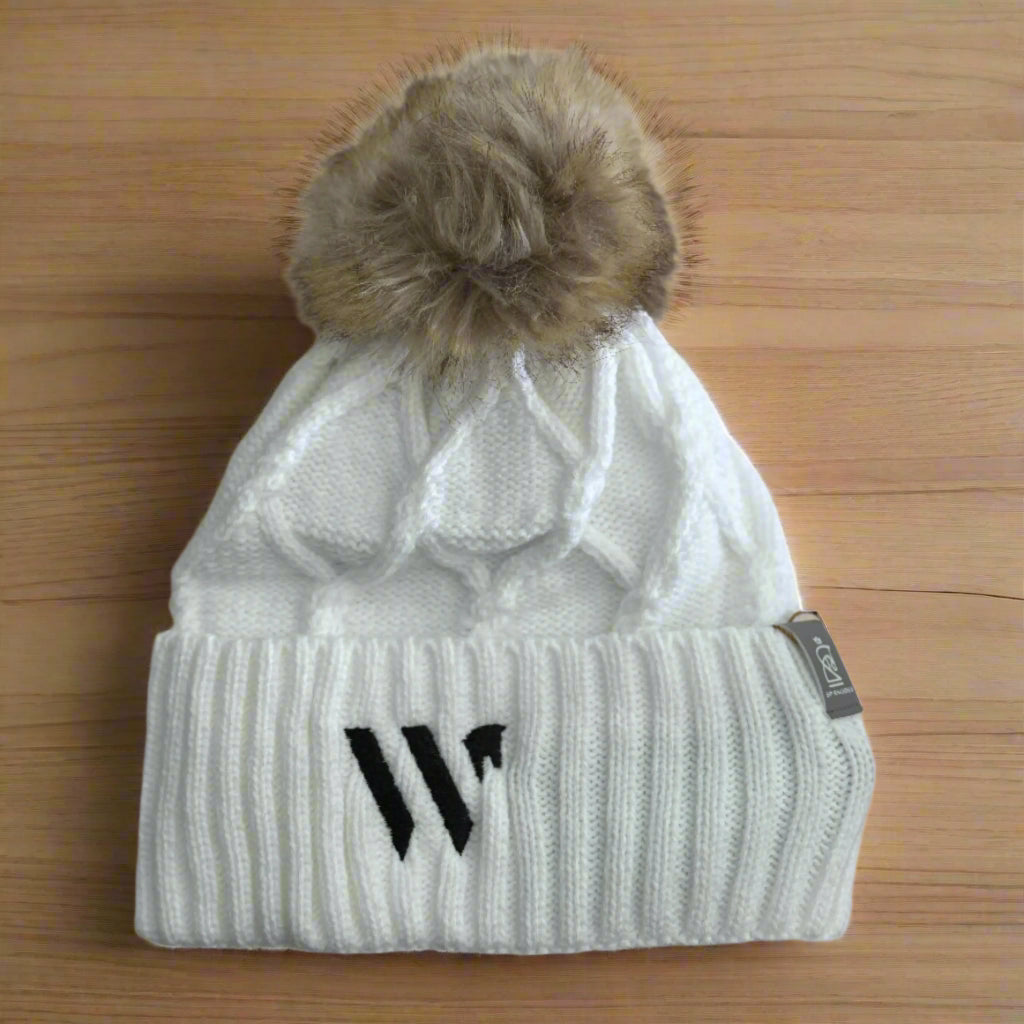 White knit beanie with fur pom-pom and logo on a beige background