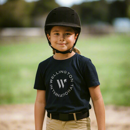 Kid wearing a black helmet and navy t-shirt with Wellington International logo outdoors