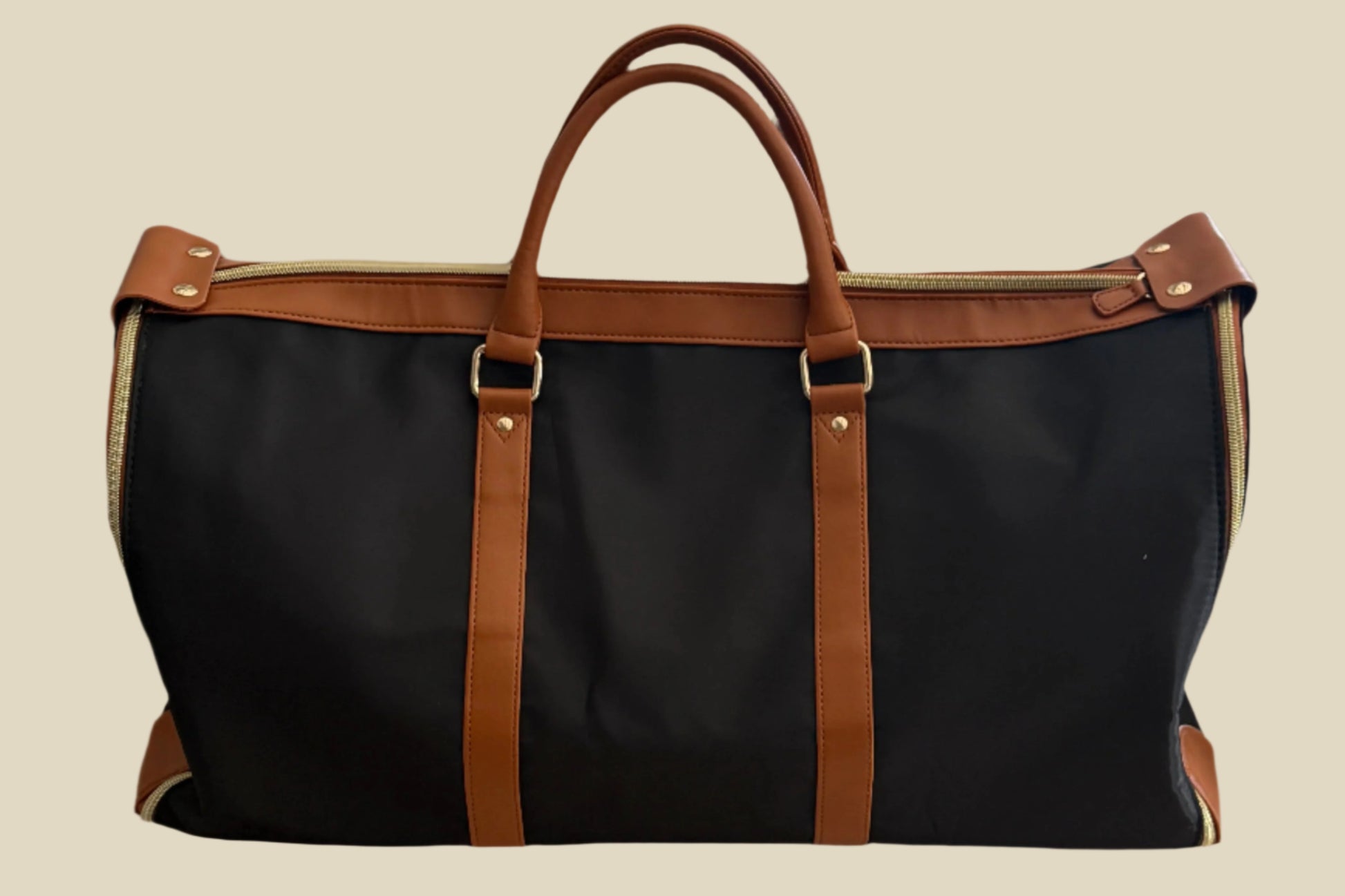 Black duffel bag with brown leather straps on a tan surface